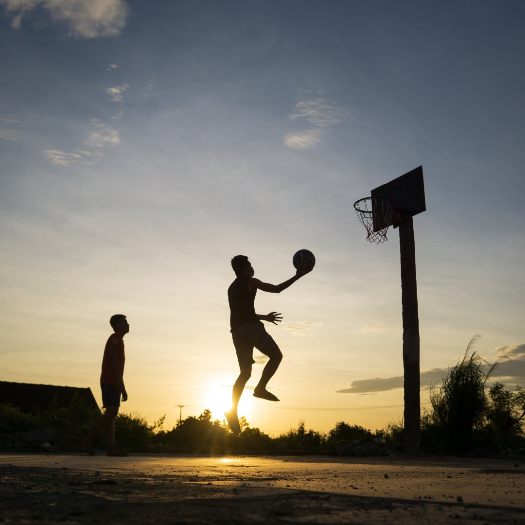 Two people playing basketball at sunset on an outdoor court.